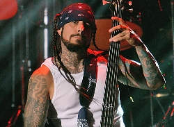 Un músico metalero con su guitarra tiene tatuajes trenzas y barba
