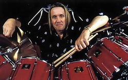 Un baterista muy sonriente con sus baquetas en la mano apoyado en sus tambores