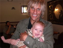 Un músico con pelo canoso con cara alegre que lleva en brazos a un bebé muy sonriente 
