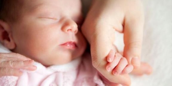UN bebe duerme plácidamente tomado de la mano con su madre