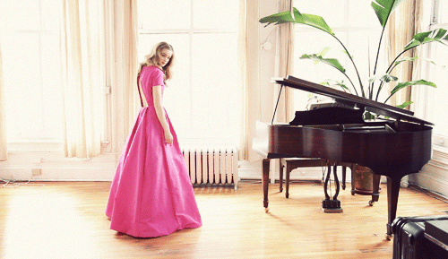 Una mujer rubia con un elegante vestido fucsia que va hacia un piano 