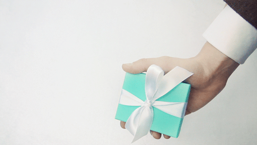 Una mano de hombre con traje que sostiene una pequeña caja de regalo con un moño