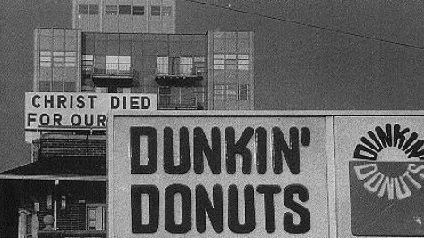 Vemos unas pgrandes letras que dicen Dios murio por vosotros y  al lado un   logo de  Dunkin donuts  