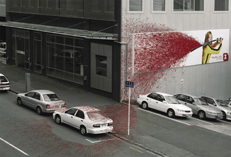 Sobre el costado de un edificio vemos una mujer con  una manguera sopla y sale  una enorme cantidad  de liquido rojo pintando la pared 