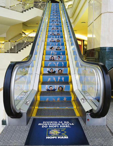 Vemos una escalera electrica que tiene una publicidad pintada en la parte interior de la escala y al final alllegar dice diviertase en la montaña rusa