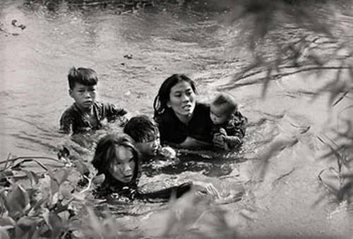 Vemos una mujer oriental con unos pequeños niños que atraviesan  un rio para pasar ala otra orilla