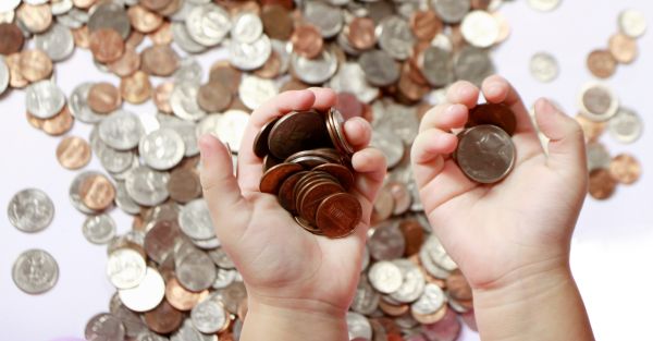 Unas manos sosteniendo montones de monedas y muchas mas al fondo