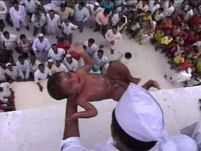 Vemos a muchisimas personas todas vestidas de blanco y un hombre desde una parte alta va lanzar un niño 