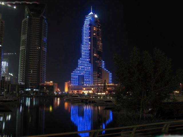 Podemos apreciar dos rascacielos en la noche y sus estructuras se reflejan en el agua
