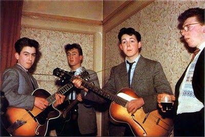 Cuatro jóvenes con traje elegante con sus guitarras bajo y otro toma algo