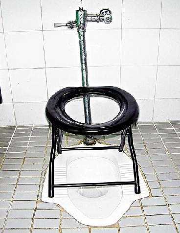 Vemos un sanitario de piso donde la colocaron una silla para comodidad y le acodicionaro el agua que cae por un tubo