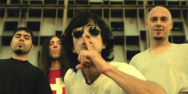 Una banda de rock con cuatro músicos y uno de ellos con gafas hace la seña de silencio