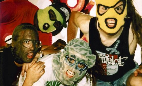 Cuatro intérpretes de una banda con máscaras grotescas que miran a la cámara