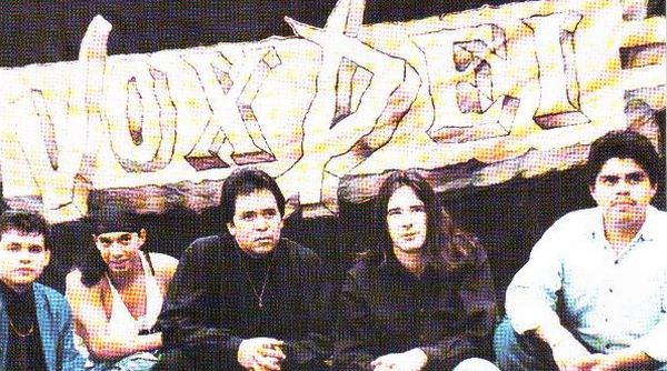 Una banda con cinco integrantes detrás de un cartel con el nombre de la banda 