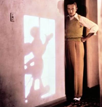 Vemos aun hombre  con camisa y chaleco que observa algo y tiene una mano en su cintura