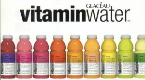 Vemos una cantidad de botellas de colores donde dice agua con vitaminas