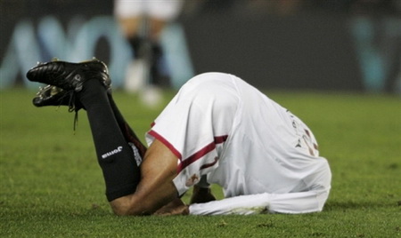 Vemos aun jugador de fútbol que se queda en la gramilla de rodillas con la cabeza  guardada entre la camiseta y puesta en el piso