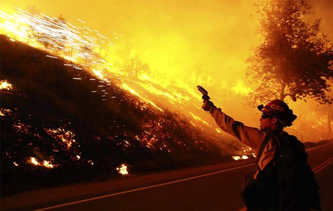 Un bombero lo vemos que lanza algo al frente se ve un color naranja de las llamas  del incendio  que se a lo,lejos 