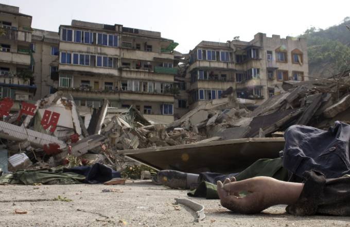Vemos a un pueblo que ha sido desbastado por un terremoto y de los escombros sobresale la mano de un cadaver