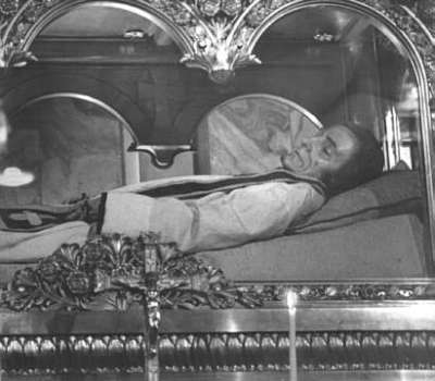 Vemos a un hombre con habito de sacerdote en un féretro de vidrio