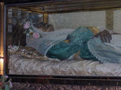 Vemos a una mujer vestida de azul con una corona de flores en la cabeza sus manos descansan una sobre la otra