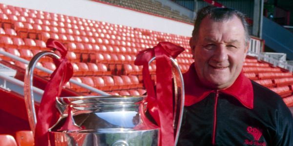 Vemos a un hombre mayor con traje de entrenador que levanta una copa dorada