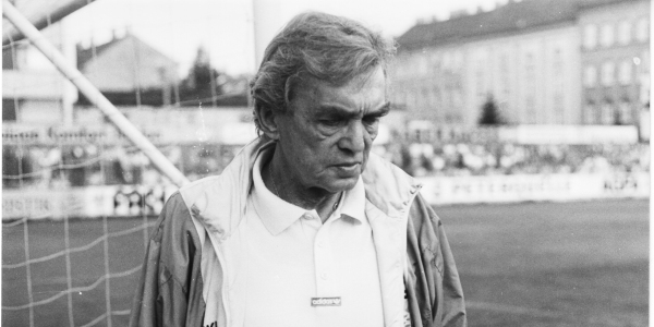 Tenemos aun hombre mayor con pelo cano  con uniforme de futbol que camina carisbajo