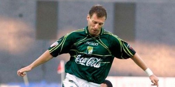 Otro futbolista rubio con uniforme verde y blanco que corre con el balón