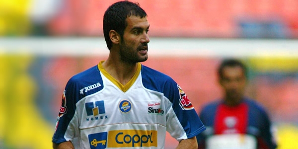 UN futbolista con uniforme blanco con azul con rostro fuerte avanza por la cancha