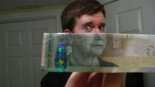Vemos a una persona con un dolar canadiense  la foto de el lo igualan con el rostro