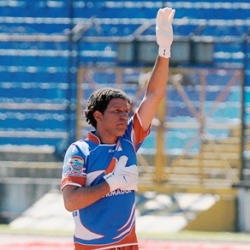 Un jugador con su uniforme levanta su mano enguantada y la otra la lleva a su pecho
