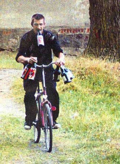 Hay un hombre sobre una bicicleta que lleva en sius manos varias  botellas de vino y  trata de sostenerse