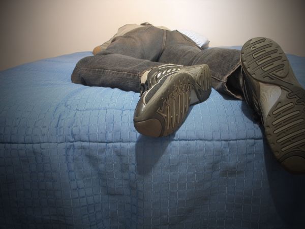 Vemos a una persona acostada en una cama con zapatos