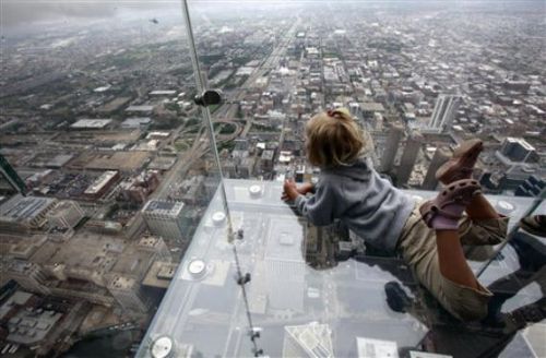 Aqui tenemos una persona tirada sobre el vidrio mira hacia abajo y alli se ve una ciudad