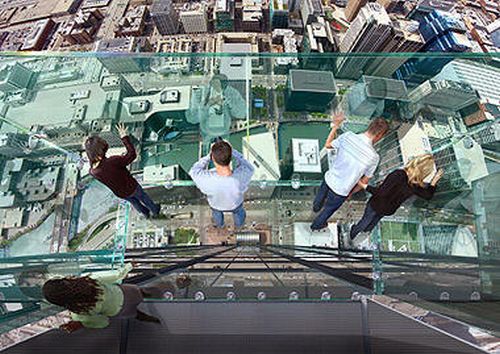 Hay cuatro personas que toman fotos desde  el vidrio y abajo se ve una ciudad