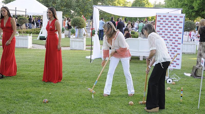 Vemos a dos mujeres tratando de introducir una pelota en un agujero y otras dos de vestido rojo miran la jugada