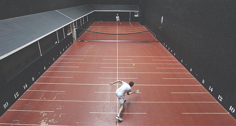Tenemos iuna cancha de color rojo con lineas y números con una valla en la mitad y los jugadores a lados opuestos
