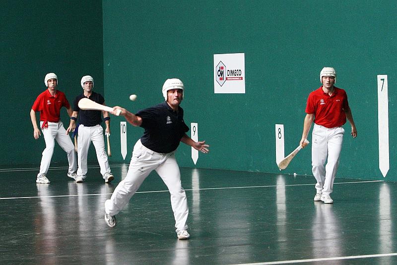 Vemos a varios jugadores con uniforme y cascos sobre un piso tiene números y lineas y con una pequeña pelota que la impulsan con paletas