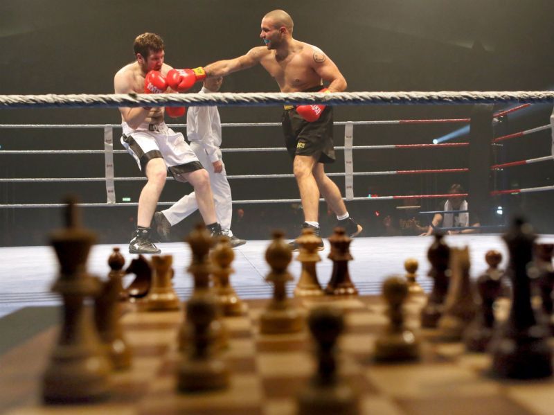 Foto de un ajedrez y atrás un rin con dos personas boxeando