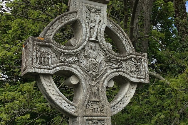 Una escultura en forma de cruz con personas talladas en las puntas y el centro