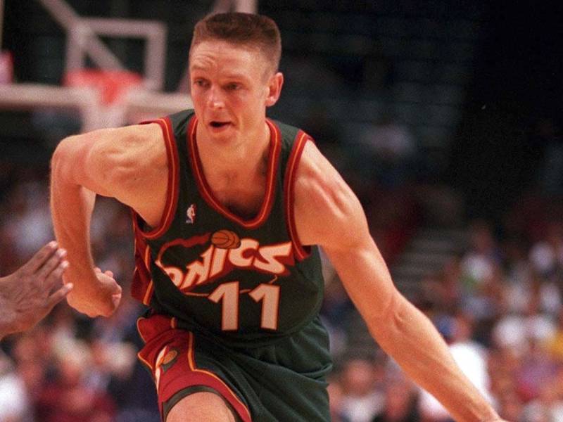 Hombre de piel blanca con uniforme de baloncesto negro y rojo, aparentemente driblando