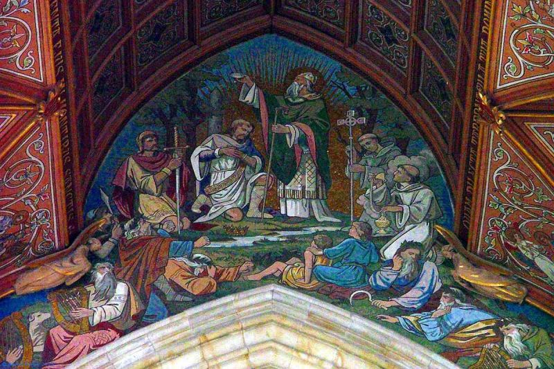 Varias personas arrodilladas al rededor de un hombre parado con una vara 