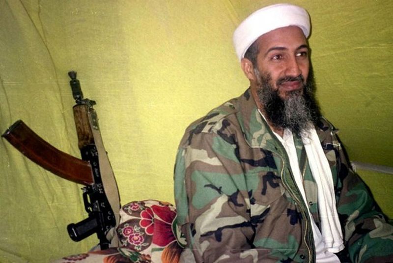 Foto de un hombre barbado con un arma al lado