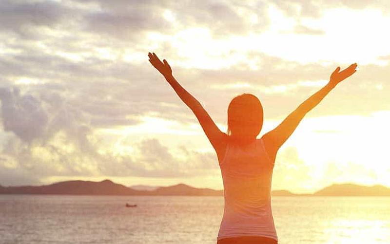 Vemos a una persona que levanta sus manos frente al mar admirando todo