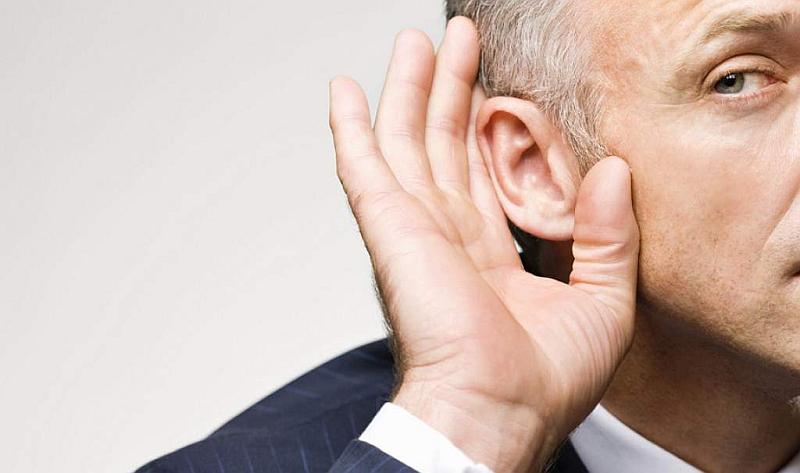 Un hombre canoso coloca su mano en su oído para escuchar mejor