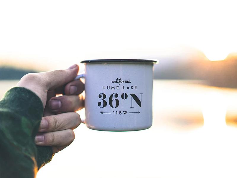 Vemos la mano de un hombre que sostiene  un pocillo donde se lee california lago hume a 36 grados norte  y abajo dice 118 oeste