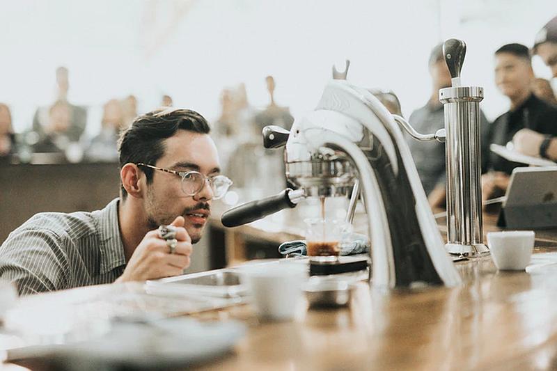 Vemos un hombre joven con gafas que observa una maquina mientras cae e l café