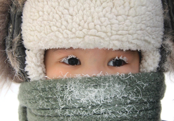 Vemos a una pequeña niña cubierta toda donde sus pestañas estan cubiertas de nieve