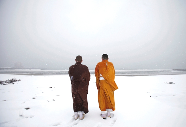 Vemos a dos monjes budistas con sus habitos que oran sobre una gran  capa de hielo