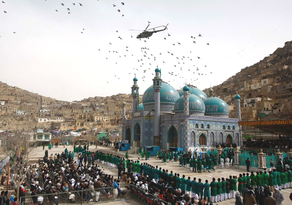 Vemos una mesquita en azulejos azules donde a su alrededor se concentran cantidades de personas en celebración de algo mientras un helicóptero sobrevuela sobre el sitio 